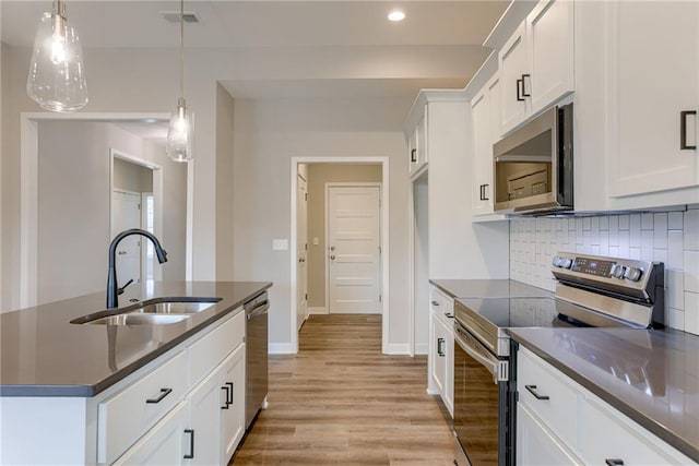 kitchen featuring appliances with stainless steel finishes, dark countertops, a sink, light wood-style floors, and backsplash