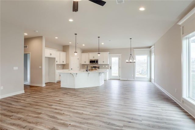 kitchen featuring stainless steel microwave, light wood-type flooring, white cabinetry, a breakfast bar, and recessed lighting