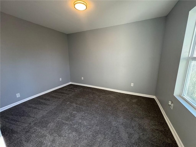 empty room featuring dark colored carpet and baseboards