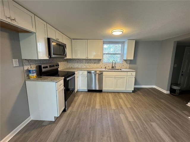 kitchen featuring stainless steel appliances, a sink, wood finished floors, baseboards, and backsplash