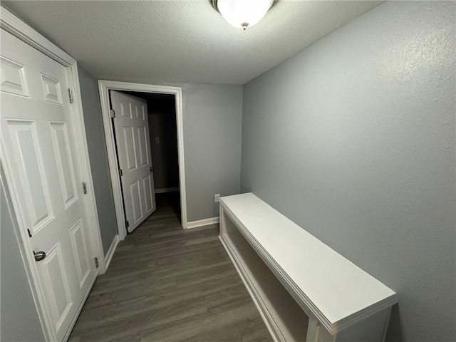 corridor with a textured ceiling, dark wood-type flooring, and baseboards