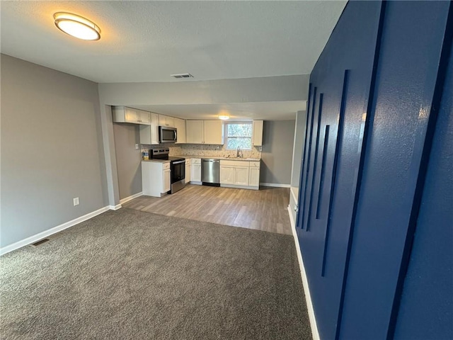 kitchen featuring appliances with stainless steel finishes, white cabinetry, baseboards, and light colored carpet