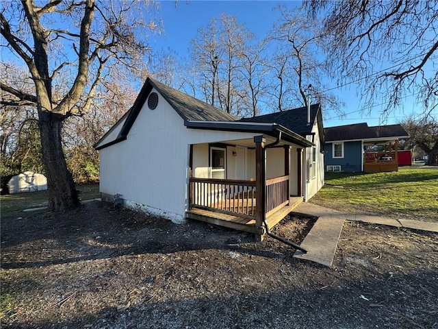 view of side of home featuring covered porch and a shingled roof