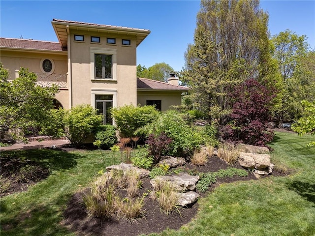 back of house featuring stucco siding, a yard, and a chimney