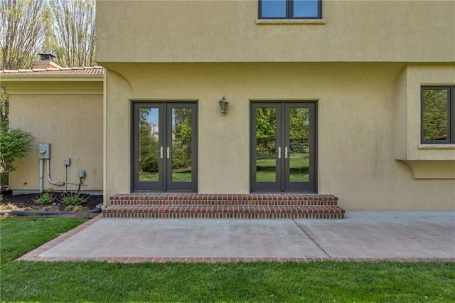 entrance to property featuring french doors, stucco siding, metal roof, and a chimney