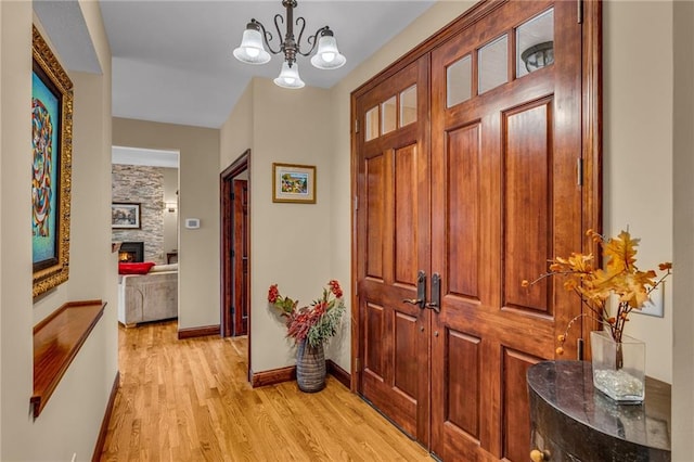 hall featuring light wood finished floors, baseboards, and a chandelier