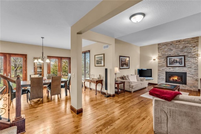 living room with light wood-style floors, a stone fireplace, a chandelier, and baseboards