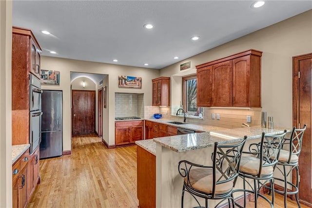 kitchen with a sink, a peninsula, appliances with stainless steel finishes, light wood finished floors, and light stone countertops