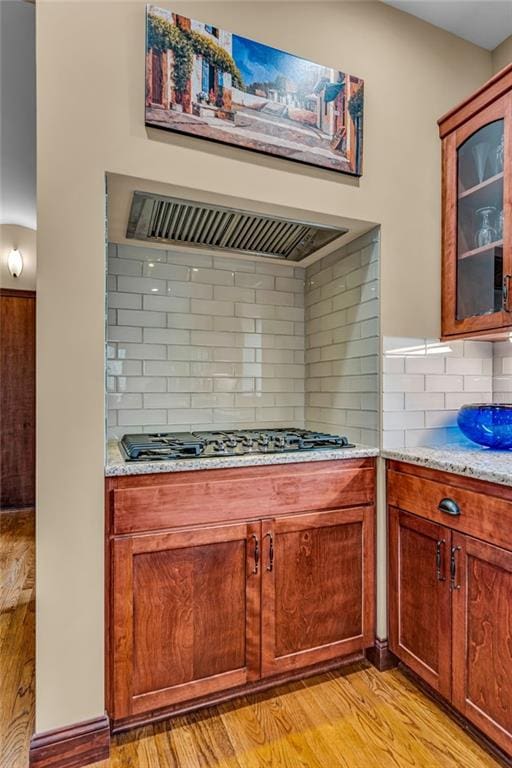 kitchen with gas stovetop, decorative backsplash, glass insert cabinets, extractor fan, and light stone counters