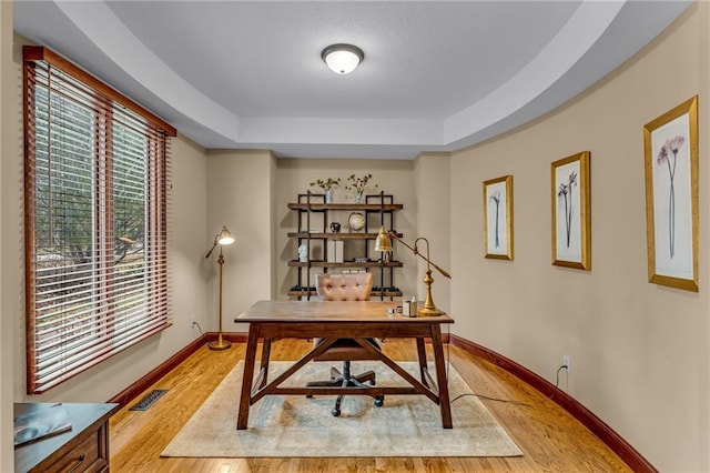 office area with light wood-type flooring, baseboards, and a tray ceiling