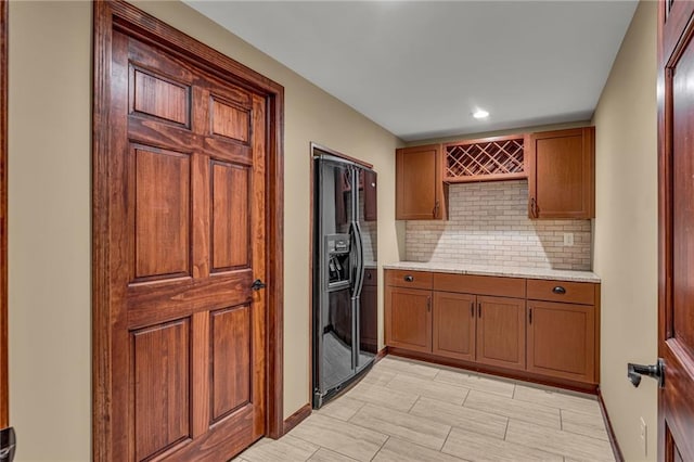 kitchen with backsplash, baseboards, recessed lighting, brown cabinetry, and light stone counters