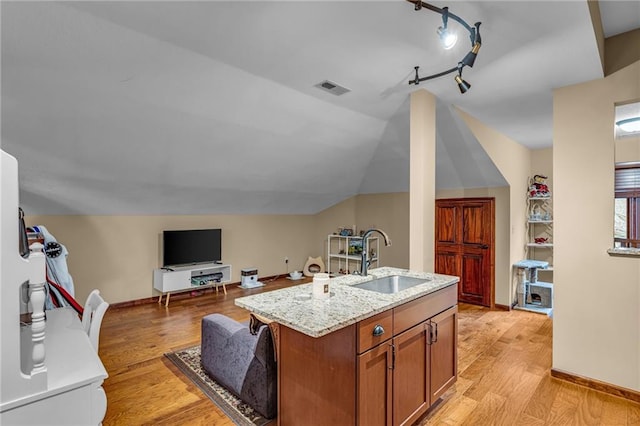 kitchen with a sink, light stone counters, light wood finished floors, brown cabinets, and lofted ceiling