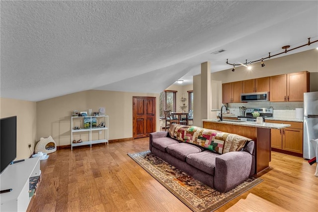 living room with light wood-style floors, a textured ceiling, track lighting, and lofted ceiling