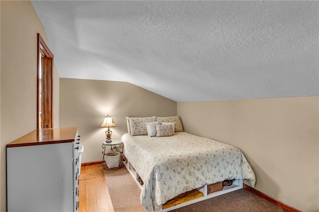 bedroom featuring lofted ceiling, a textured ceiling, baseboards, and light wood-style floors