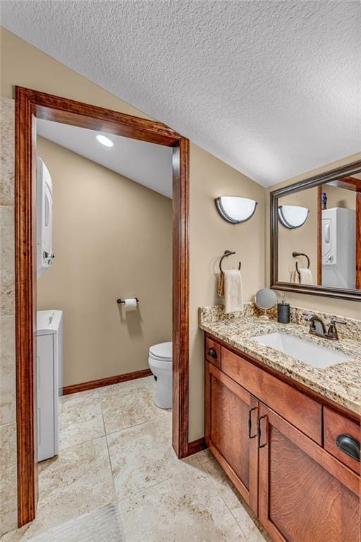 bathroom featuring toilet, stacked washer / dryer, lofted ceiling, vanity, and a textured ceiling