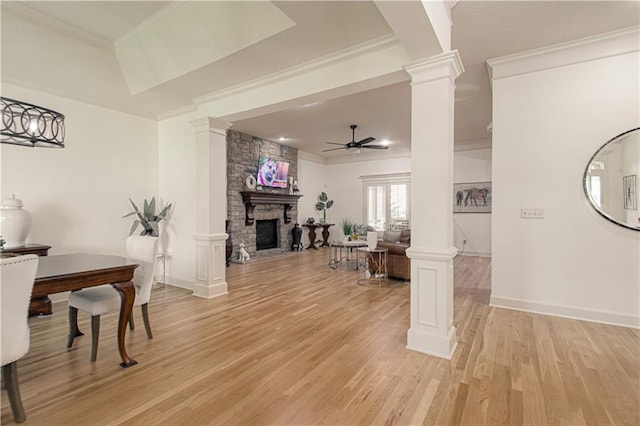 living area with ornate columns, a ceiling fan, a stone fireplace, light wood-style flooring, and crown molding