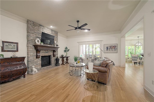 living room featuring light wood finished floors, ceiling fan, crown molding, a stone fireplace, and baseboards