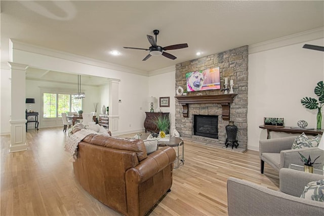 living room with decorative columns, light wood-style flooring, a ceiling fan, a stone fireplace, and ornamental molding