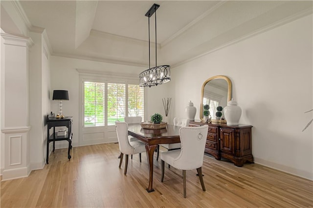 dining space with light wood-style floors, a chandelier, a raised ceiling, crown molding, and ornate columns