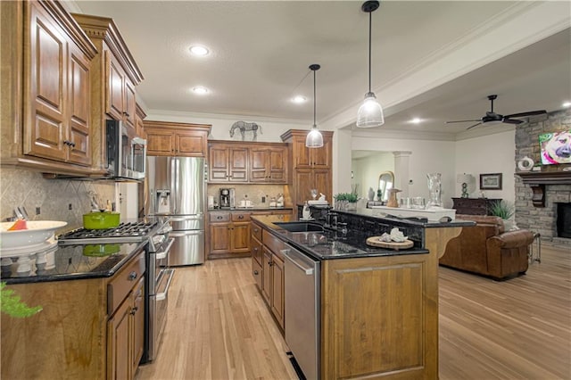 kitchen with appliances with stainless steel finishes, brown cabinetry, light wood-style floors, a ceiling fan, and a breakfast bar