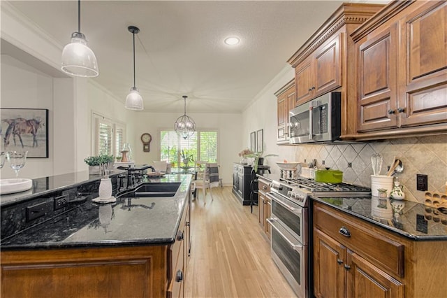 kitchen with stainless steel appliances, a sink, crown molding, light wood finished floors, and dark stone countertops