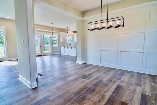 7812 N Spruce Ave, Kansas City, MO 64119 - unfurnished dining area featuring a chandelier, a decorative wall, plenty of natural light, and dark wood-type flooring
