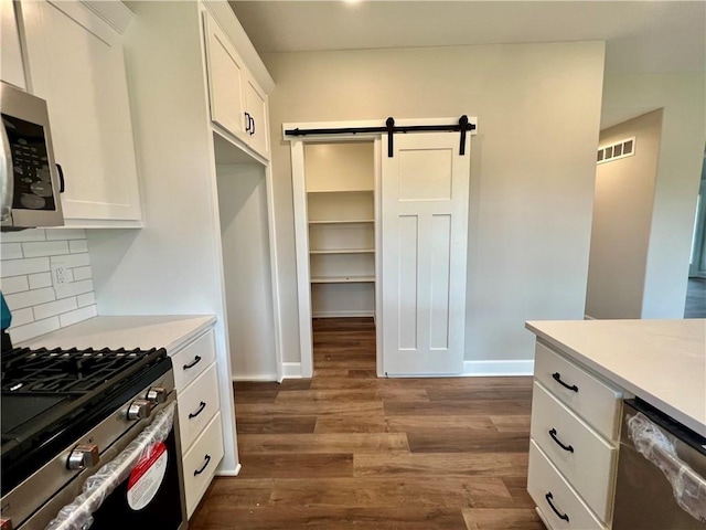 7812 N Spruce Ave, Kansas City, MO 64119 - kitchen with appliances with stainless steel finishes, a barn door, white cabinets, backsplash, and light countertops