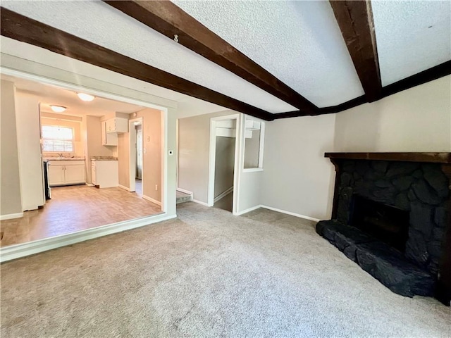 11914 E 59th Ter, Kansas City, MO 64133 - unfurnished living room with light carpet, beam ceiling, baseboards, a textured ceiling, and a fireplace