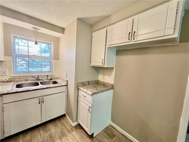 11914 E 59th Ter, Kansas City, MO 64133 - kitchen featuring light wood finished floors, a sink, white cabinetry, decorative backsplash, and light countertops