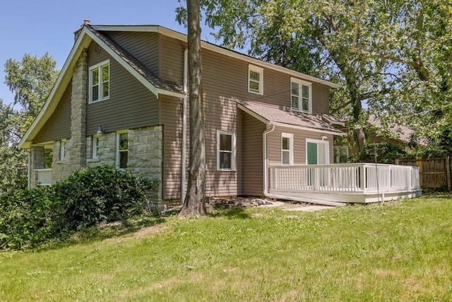back of house featuring a wooden deck, a yard, stone siding, and a shingled roof