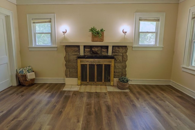 unfurnished living room with crown molding, baseboards, wood finished floors, and a stone fireplace