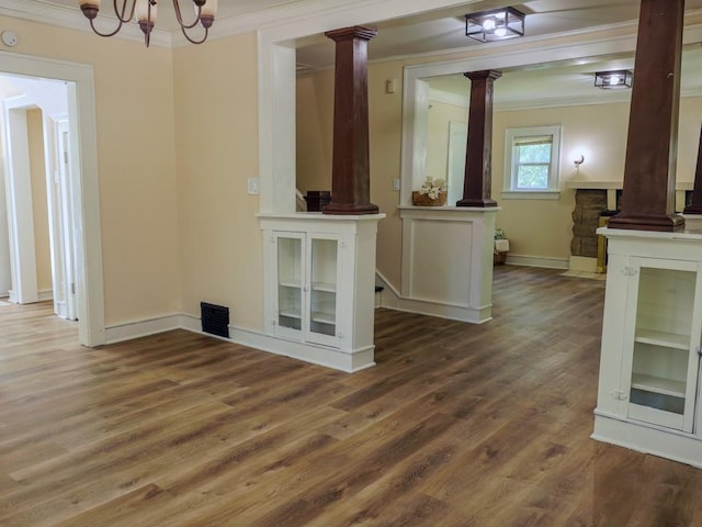 unfurnished dining area featuring ornate columns, crown molding, wood finished floors, a chandelier, and baseboards