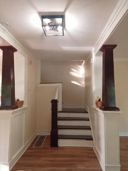 staircase with ornate columns, wood finished floors, and baseboards
