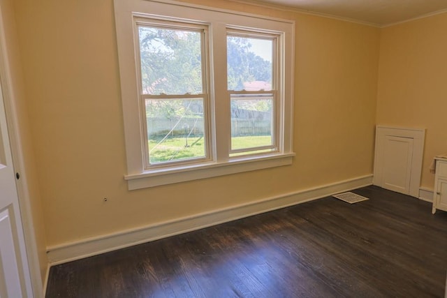 empty room featuring plenty of natural light, dark wood-style flooring, crown molding, and baseboards