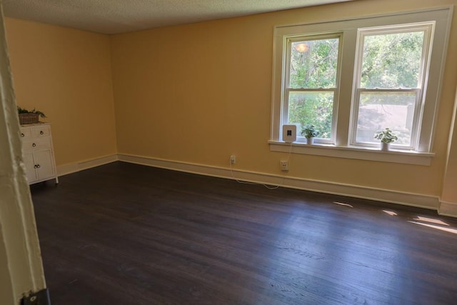 empty room with dark wood finished floors, healthy amount of natural light, baseboards, and a textured ceiling