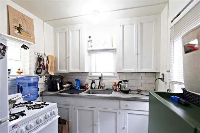 kitchen with white gas range oven, a sink, white cabinetry, and backsplash