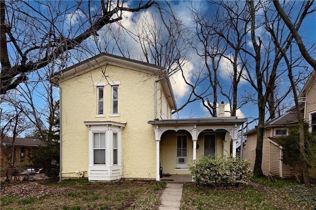 italianate house with a porch, brick siding, and a chimney