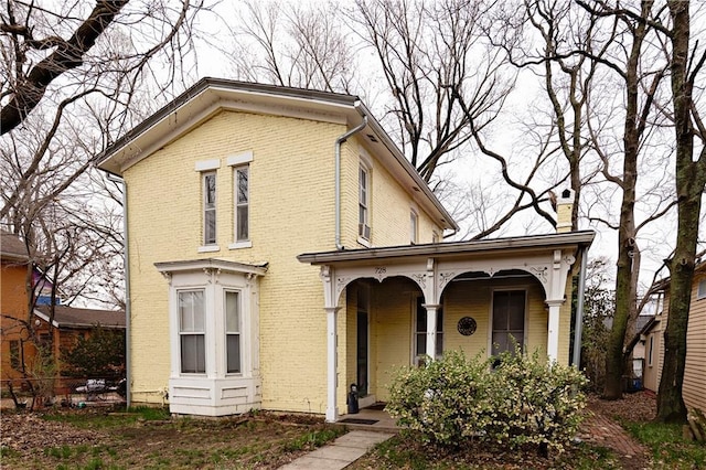 view of front of property featuring a porch, a chimney, and brick siding