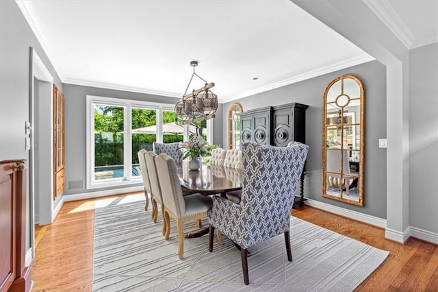 dining room featuring light wood finished floors, baseboards, crown molding, and a chandelier