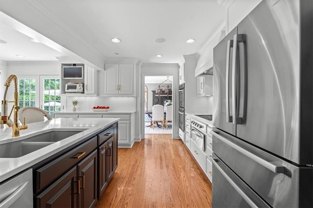 kitchen featuring appliances with stainless steel finishes, ornamental molding, a sink, light countertops, and light wood-type flooring