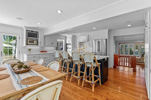 kitchen with stainless steel appliances, light wood-style flooring, light countertops, ornamental molding, and a kitchen island with sink