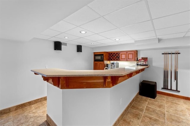 indoor wet bar with black microwave, recessed lighting, baseboards, and a paneled ceiling