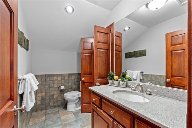 bathroom with lofted ceiling, toilet, vanity, tile walls, and wainscoting