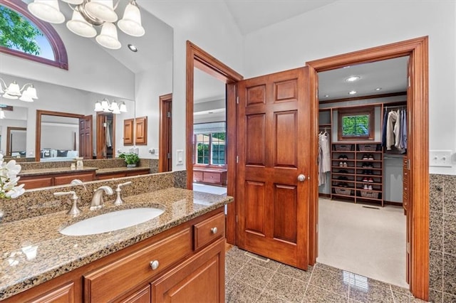 full bathroom with a chandelier, granite floors, vanity, a walk in closet, and high vaulted ceiling