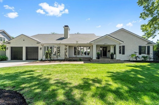 view of front of house with a chimney, an attached garage, driveway, a front lawn, and stone siding