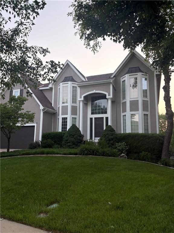 view of front facade featuring stucco siding, a lawn, and a garage