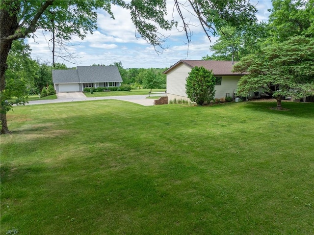 view of green lawn with a garage and driveway