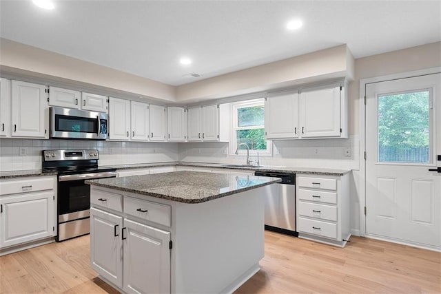 1051 E 121st St, Olathe, KS 66061 - kitchen with stainless steel appliances, dark stone countertops, white cabinets, light wood-style floors, and a kitchen island