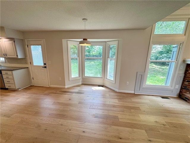 1051 E 121st St, Olathe, KS 66061 - unfurnished dining area with light wood finished floors, baseboards, healthy amount of natural light, and a textured ceiling