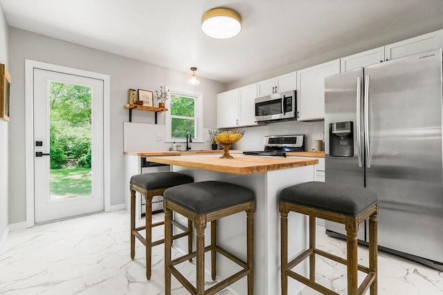 9811 Cambridge Ave, Kansas City, MO 64134 - kitchen with stainless steel appliances, butcher block counters, light marble finish flooring, a kitchen bar, and a sink
